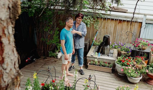 Aerial view of a therapist helping a patient stand with better alignment by adjusting the front and back of his upper body. They are standing in a garden