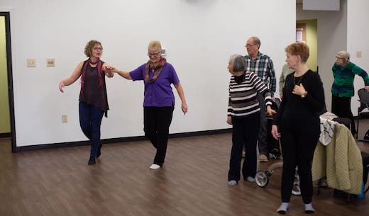 Candace walking with a patient in a dance-like position. They are side by side, hand at chest level and ahead of them. The pateint has her hand on top of Candace's.