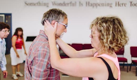 Candace facing a patient, and holding his lower skull with her hands in a gesture of neck support.