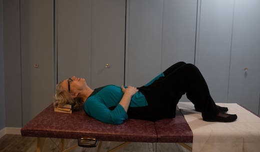 Someone laying down on a massage table with their head elevated on a wooden block.