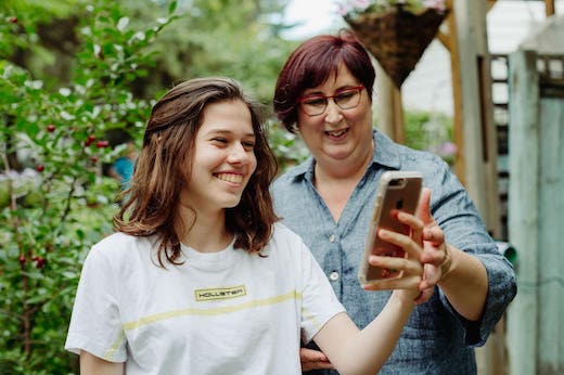 Daisy and a young person standing in a garden and looking at an iphone, both smiling.